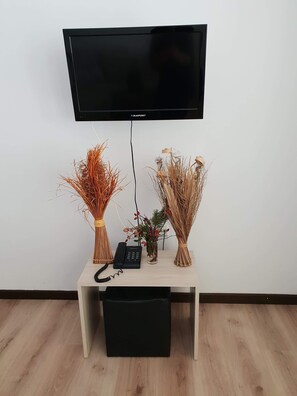 A flat-screen TV mounted on a wall above a wooden desk with a telephone and decorative plants.