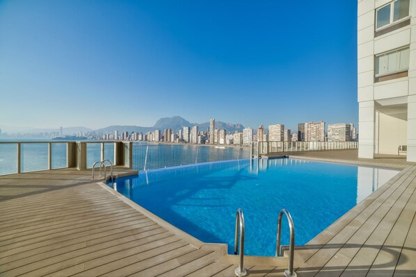 A rooftop pool with a city skyline view, wooden deck, and metal pool ladders.