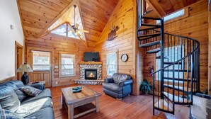 A cozy cabin interior with a fireplace, a sofa, a coffee table, and a spiral staircase.