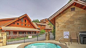 A hot tub surrounded by stone walls, with a wooden building and a sign indicating spa rules in the background.