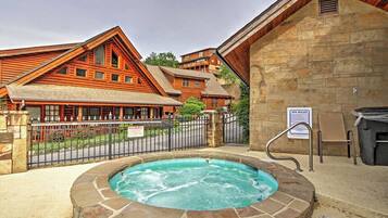A hot tub surrounded by stone walls, with a wooden building and a sign indicating spa rules in the background.