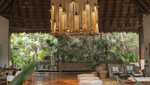 A spacious room with a high ceiling, a hanging light fixture, and a view of lush greenery outside. - Chablé Maroma (Playa del Carmen)