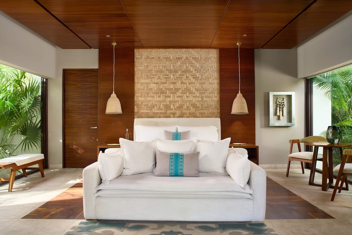 A modern bedroom with a wooden ceiling, a large bed with white bedding, and a woven wall panel.