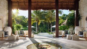 A tropical lounge with thatched roof, wicker furniture, and a central water feature. - Chablé Maroma (Playa del Carmen)