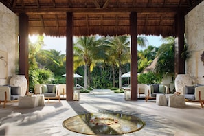 A tropical resort lobby with a thatched roof, comfortable seating, a central water feature, and a view of palm trees. - Chablé Maroma (Playa del Carmen)