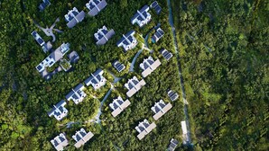 Vista aérea de un resort con múltiples alojamientos tipo bungalow rodeados de densa vegetación tropical, una playa de arena y aguas turquesas cristalinas.
