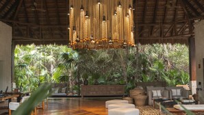 Amplia habitación con techo alto, lámpara colgante y vistas a exuberante vegetación.