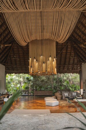 Amplia habitación con techo alto, lámpara colgante y vistas a exuberante vegetación.