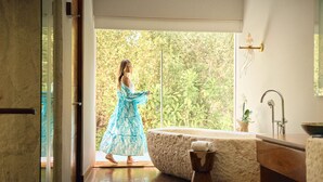 A spacious bathroom with a large bathtub, a wooden vanity, and a window with a view of greenery. - Chablé Maroma (Playa del Carmen)