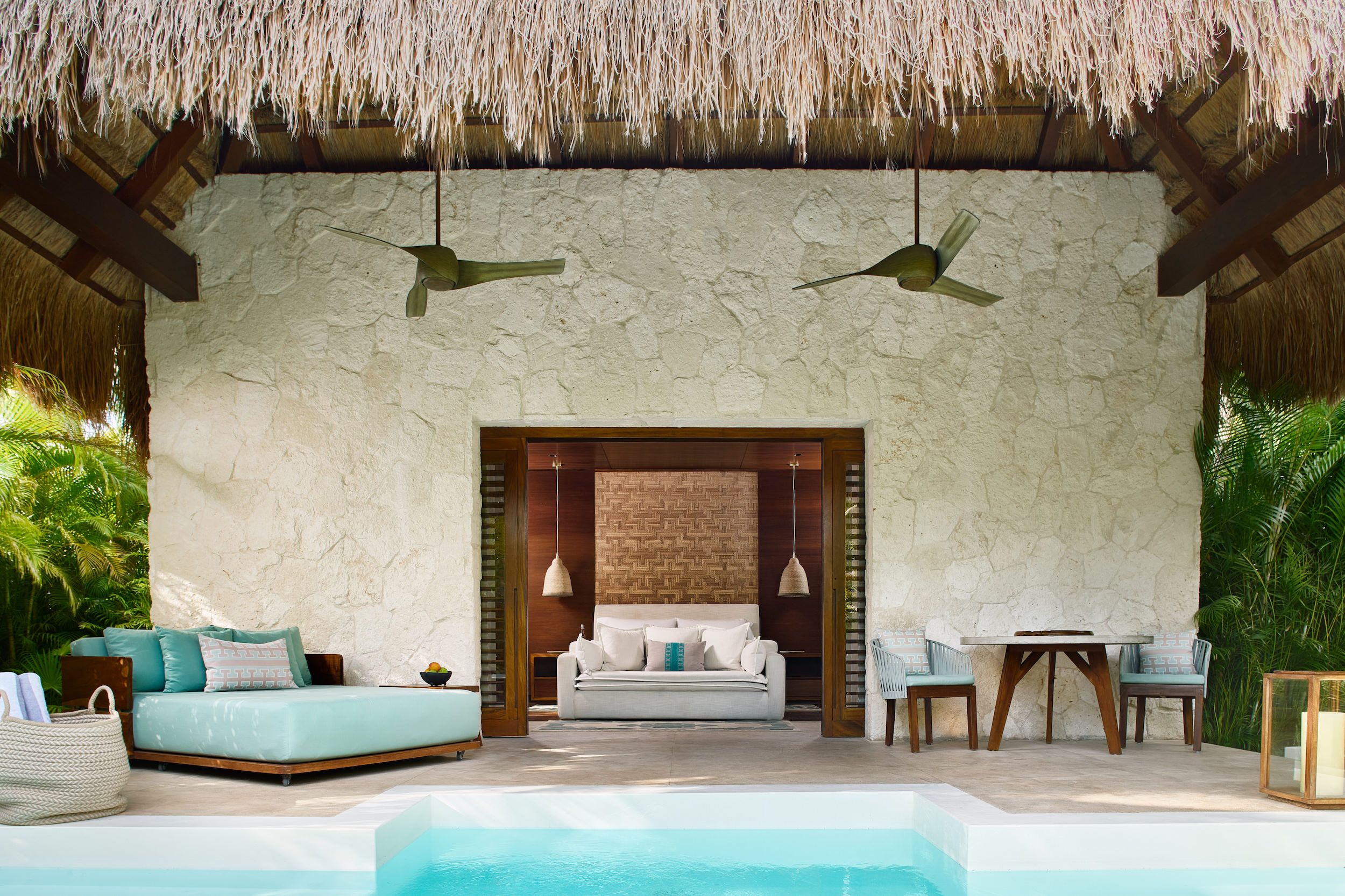 Um quarto com parede de pedra, telhado de palha, sofá, mesa e piscina.
