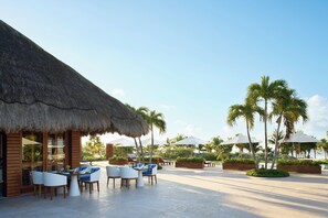 An outdoor seating area with thatched-roof structures, palm trees, and lounge chairs.