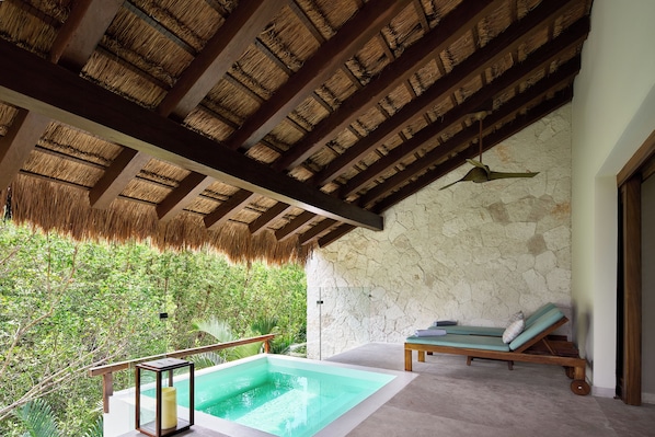 A pool area with a stone wall, a wooden ceiling, and a lounge chair.