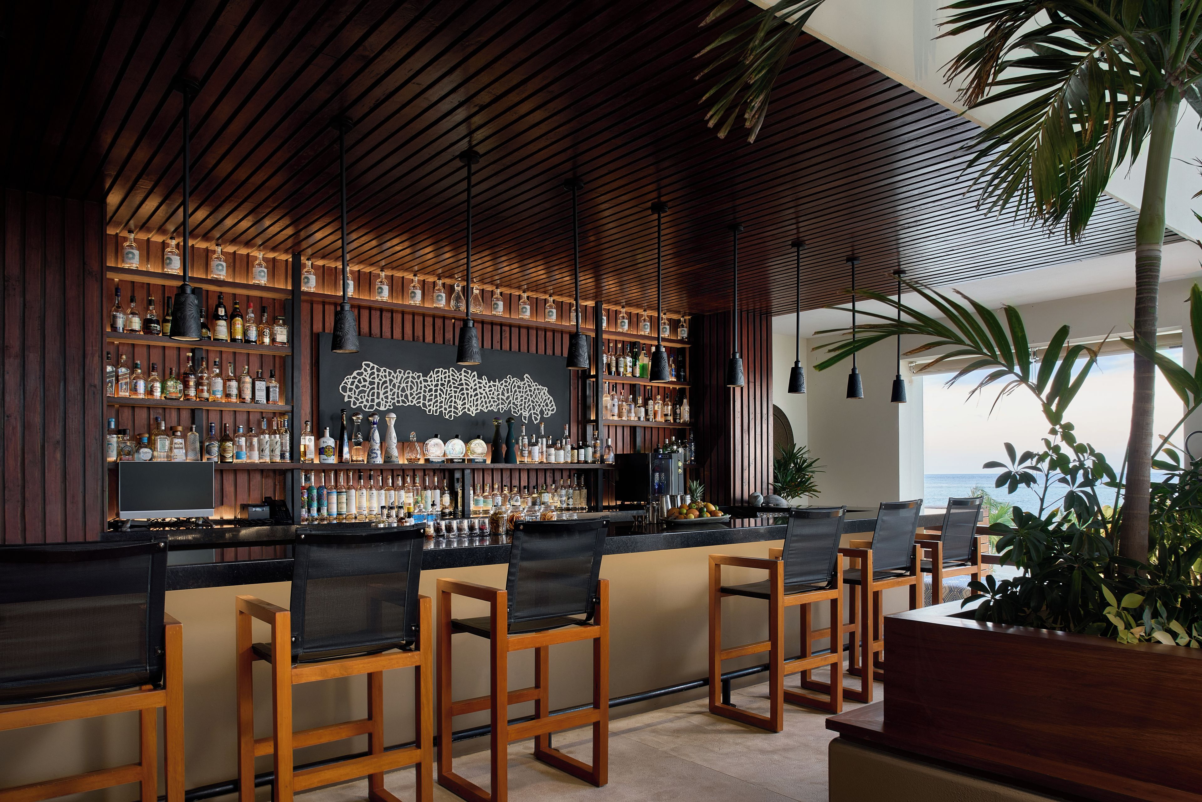 A bar area with wooden chairs, a bar counter, and shelves of bottles.