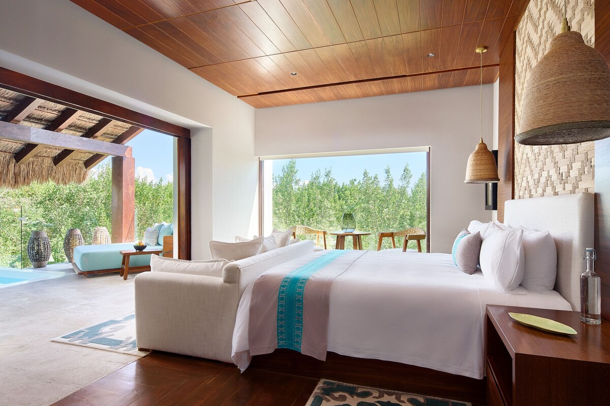 Un dormitorio espacioso con una cama grande, un sofá y vistas al verde exterior.