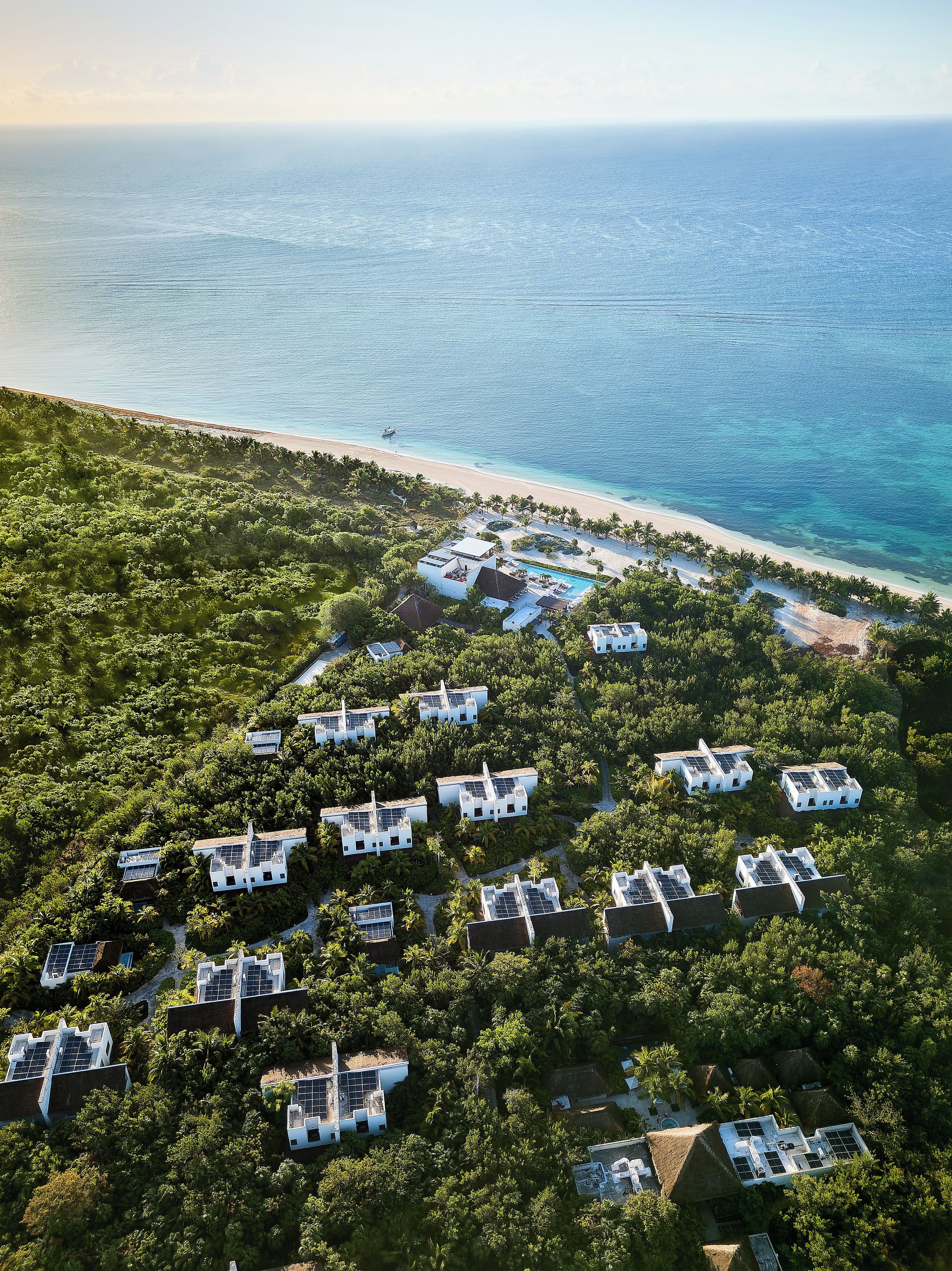 An aerial view of a resort with multiple white buildings, a beach, and a clear view of the ocean.