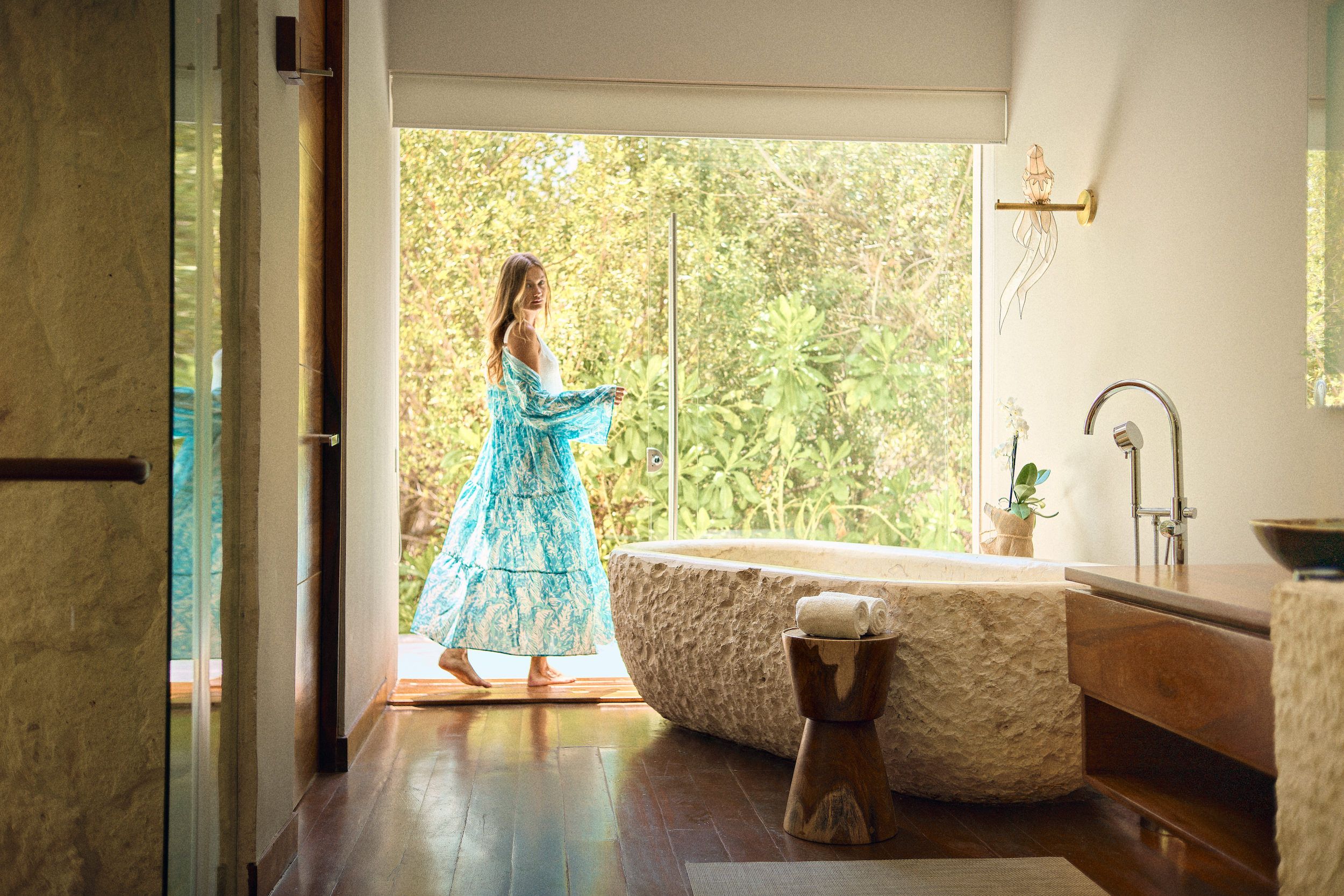 A spacious bathroom with a large bathtub, a wooden vanity, and a window with a view of greenery.