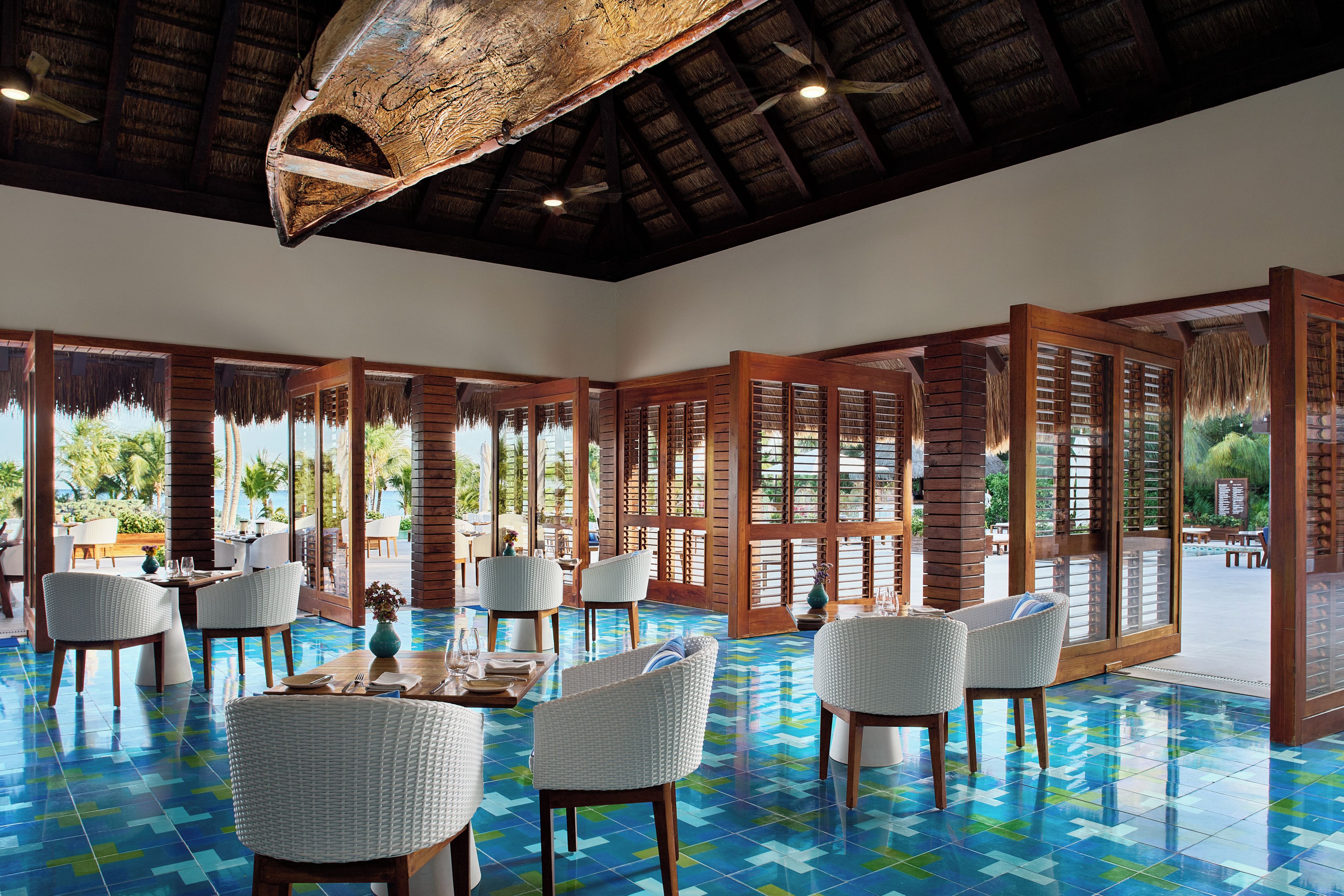 A spacious indoor area with a tiled floor, wooden furniture, and large windows allowing natural light.