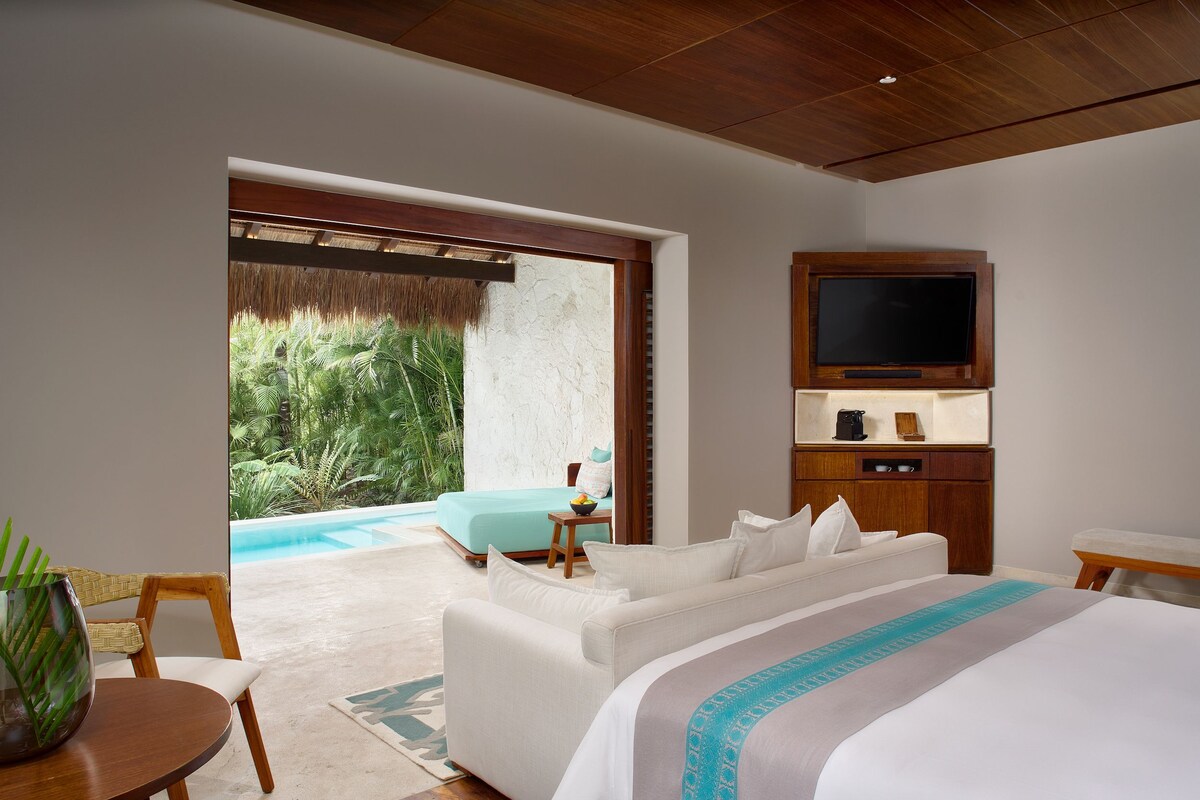 Un dormitorio con una cama grande, televisión, aparador de madera y vistas a una piscina y zonas verdes.