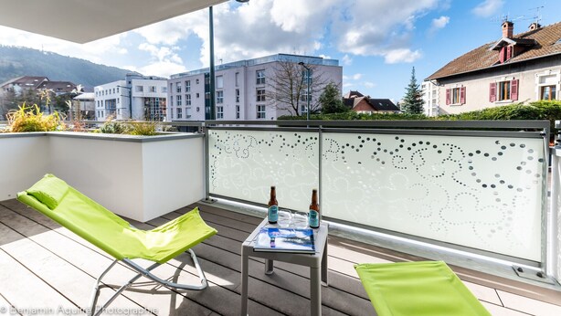 A balcony with two green lounge chairs, a table with two bottles, and a magazine.