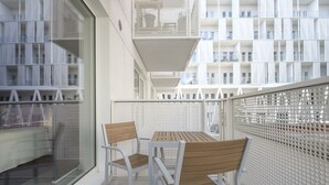 Parvekkeella on pöytä ja tuolit, ja sieltä on näkymä moderniin rakennukseen, jossa on myös parvekkeita.