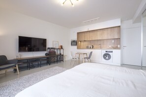 Um quarto moderno com uma cama grande, televisão, escrivaninha e kitchenette.