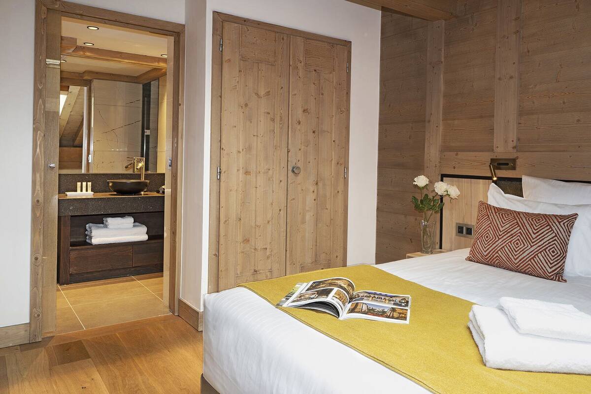 A hotel room with a wooden headboard, a bed with white linens, a bedside table with a magazine, and a wooden wardrobe.