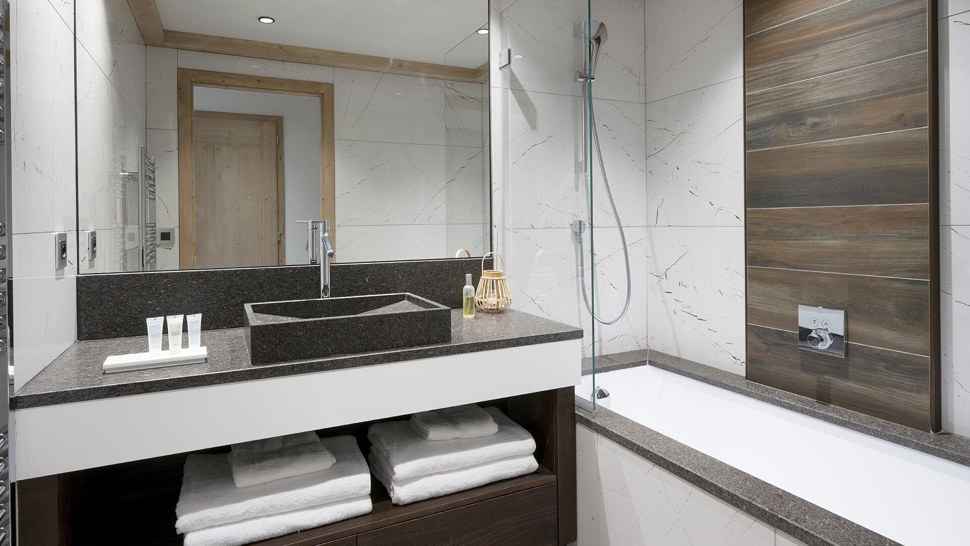A modern bathroom with a marble sink, a glass shower enclosure, and a wooden panel wall.