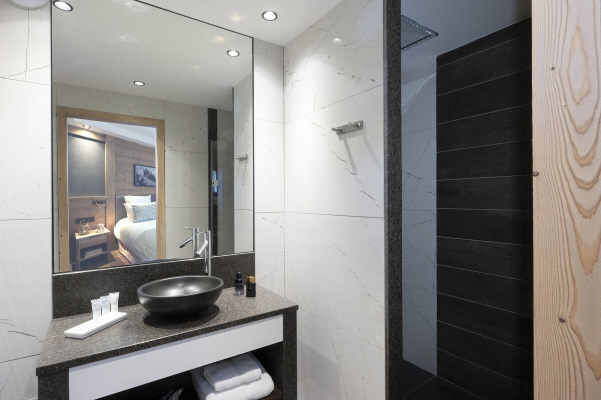 A modern bathroom with a large mirror, a black sink, and a shower area.