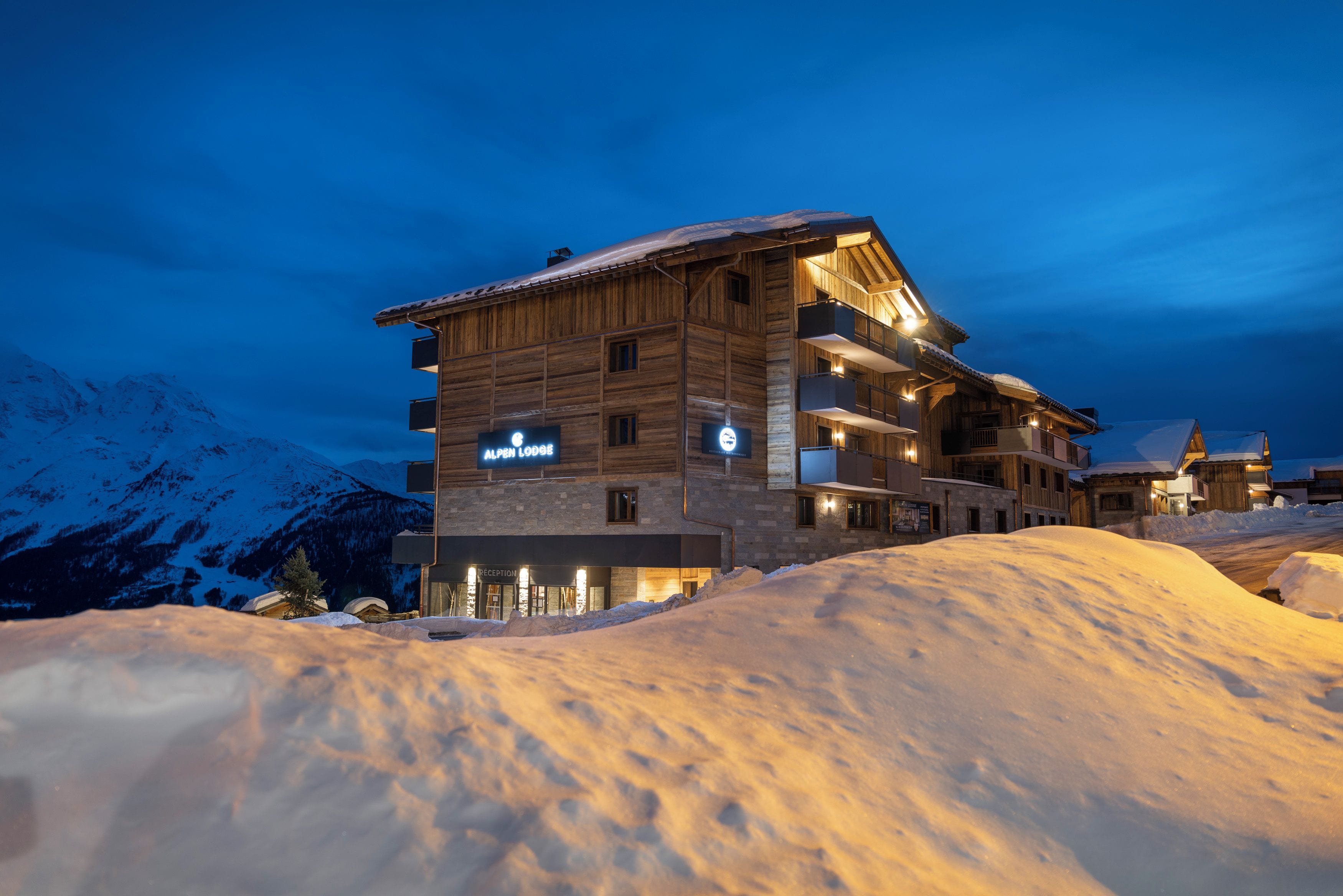 A multi-story wooden lodge with a reception area, balconies, and a sign indicating it is an alpine lodge.