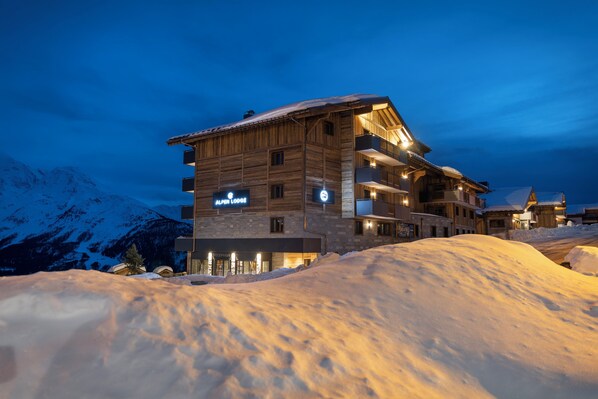 A multi-story wooden lodge with a reception area, balconies, and a sign indicating it is an alpine lodge. - MGM Hôtels & Résidences – Résidence Alpen Lodge (Montvalezan)