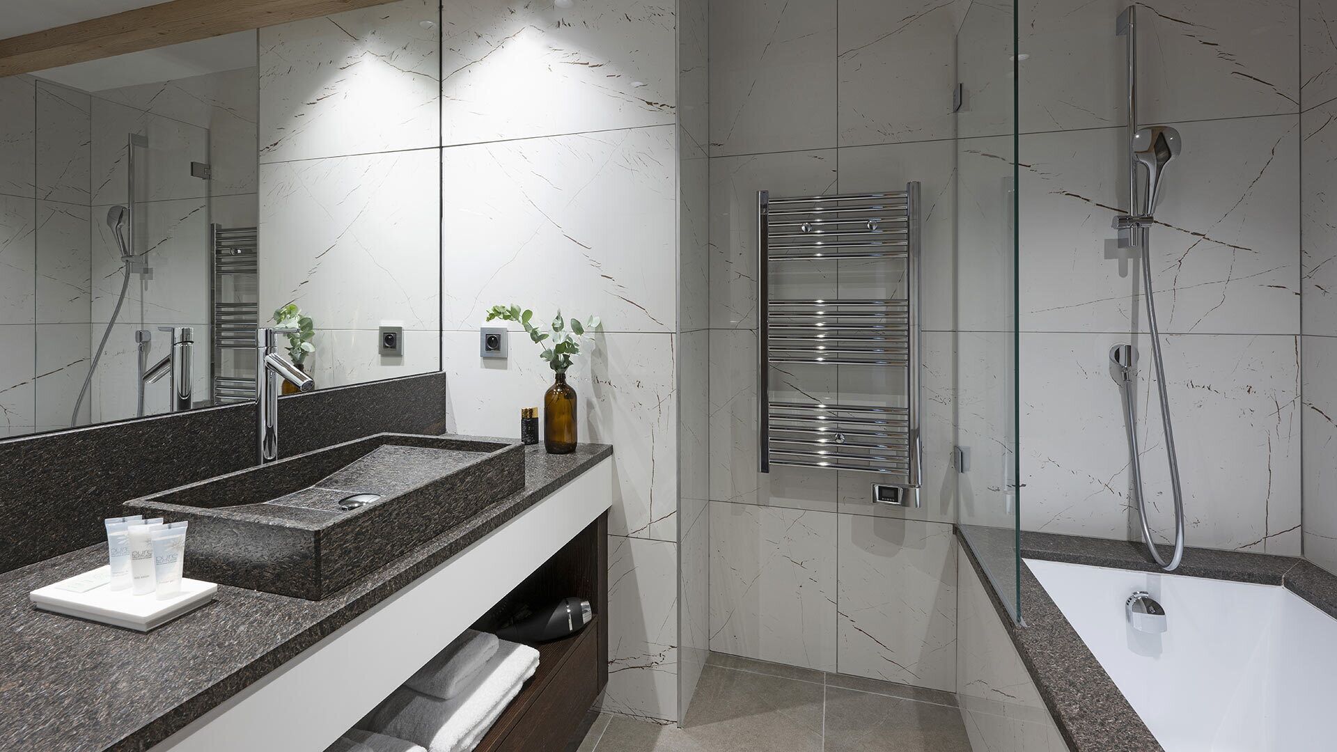 A modern bathroom with a granite countertop, a large mirror, a towel rack, and a shower area.