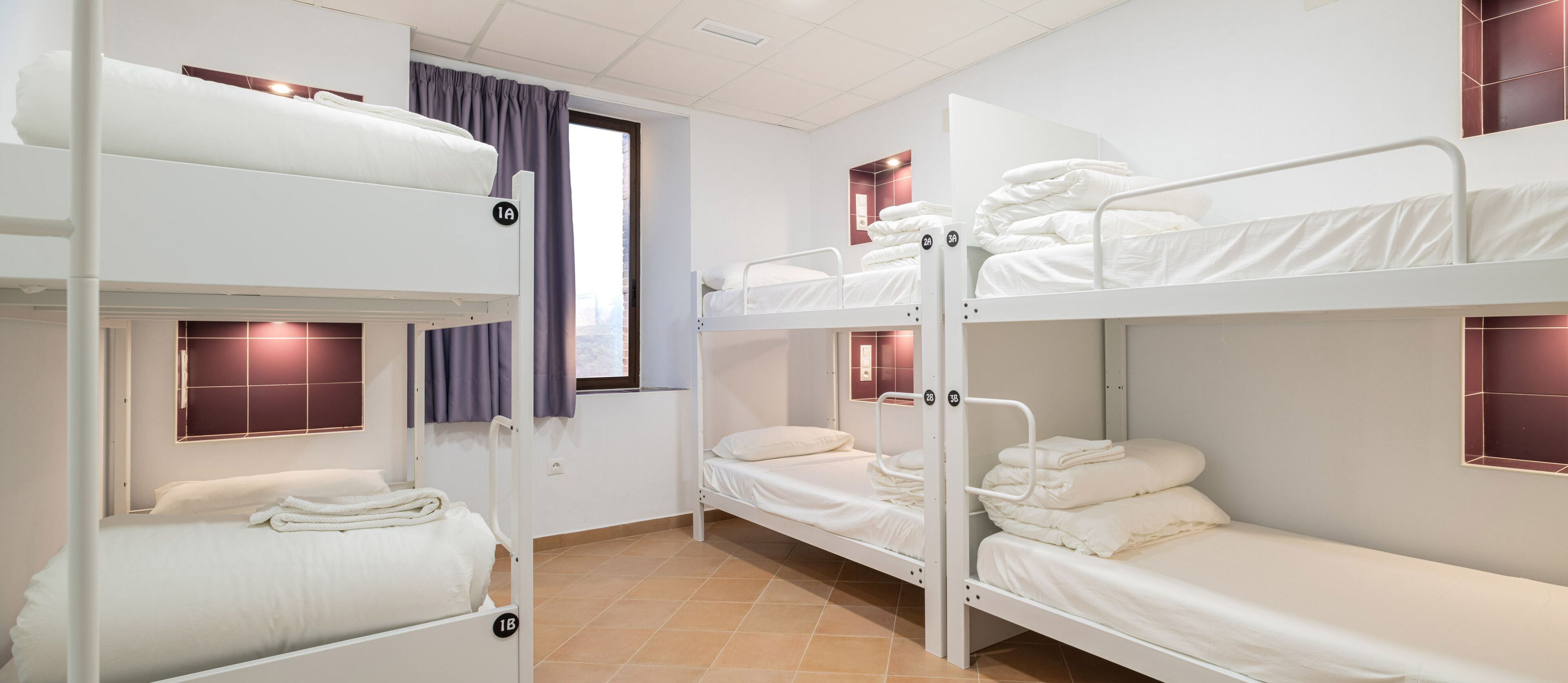 Un dormitorio con literas, una ventana con cortinas y suelo de baldosas.