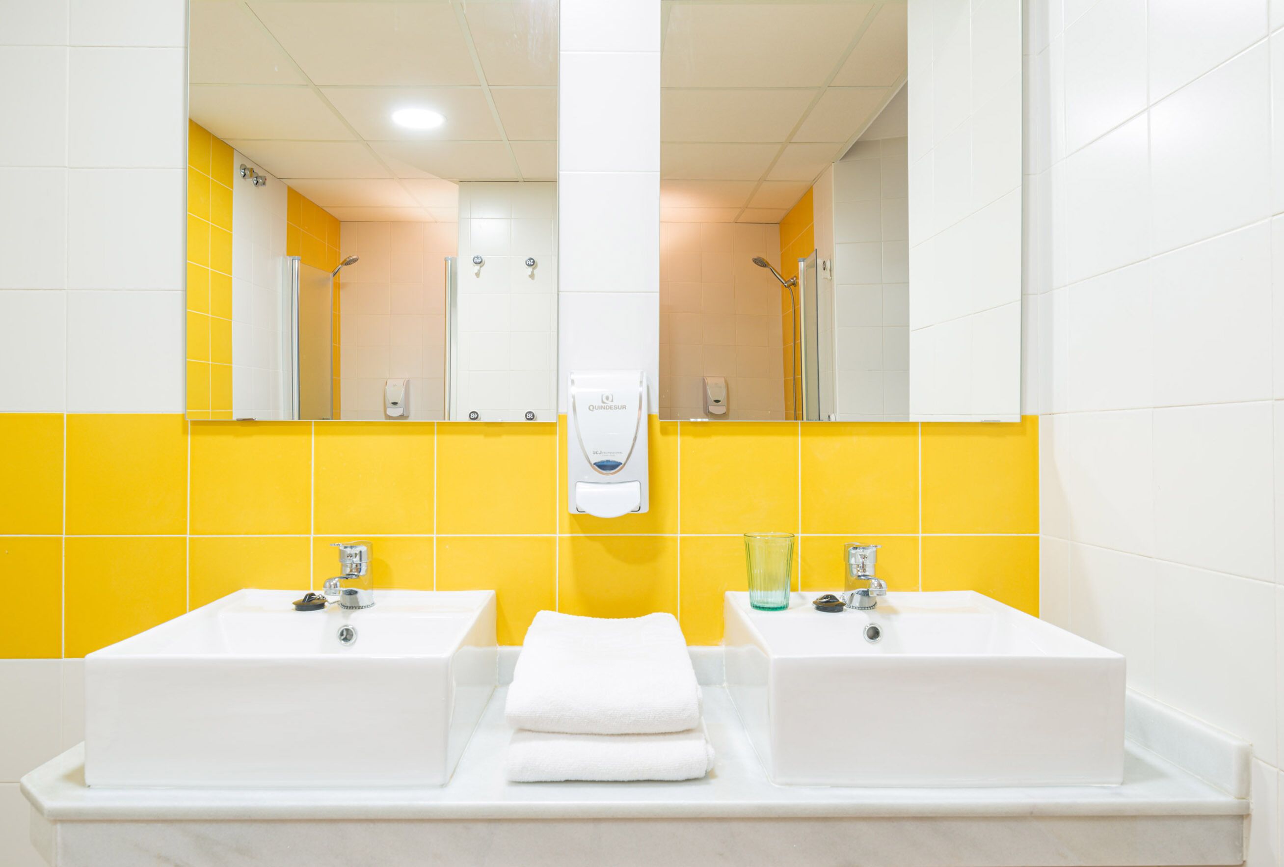 A bathroom with two sinks, a mirror, and a yellow-tiled wall.