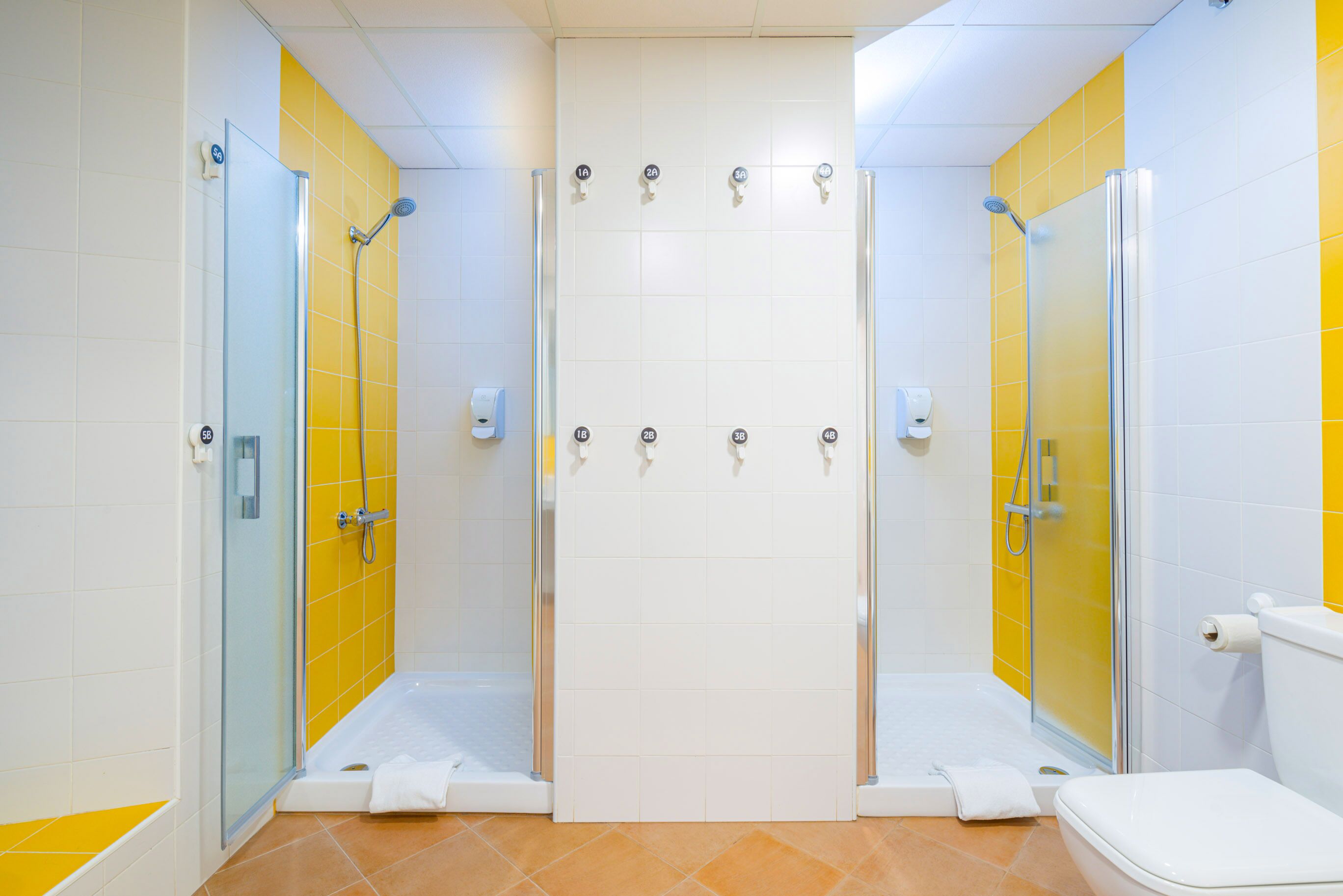Un baño con dos cabinas de ducha, un inodoro y una zona de ducha con mampara de vidrio.