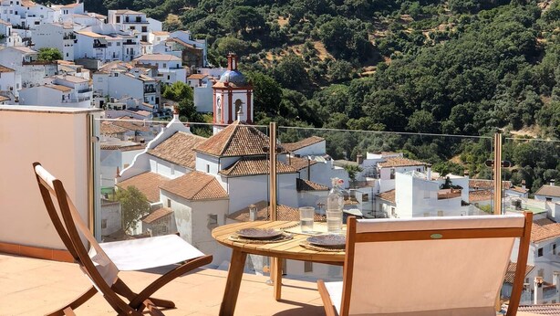 A terrace with two wooden chairs and a small table, overlooking a hillside village with white buildings and a church. - Benarrabá Hostel (Benarraba)