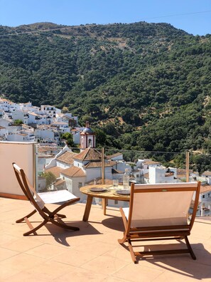 A terrace with two wooden chairs and a small table, overlooking a hillside village with white buildings and a church. - Benarrabá Hostel (Benarraba)