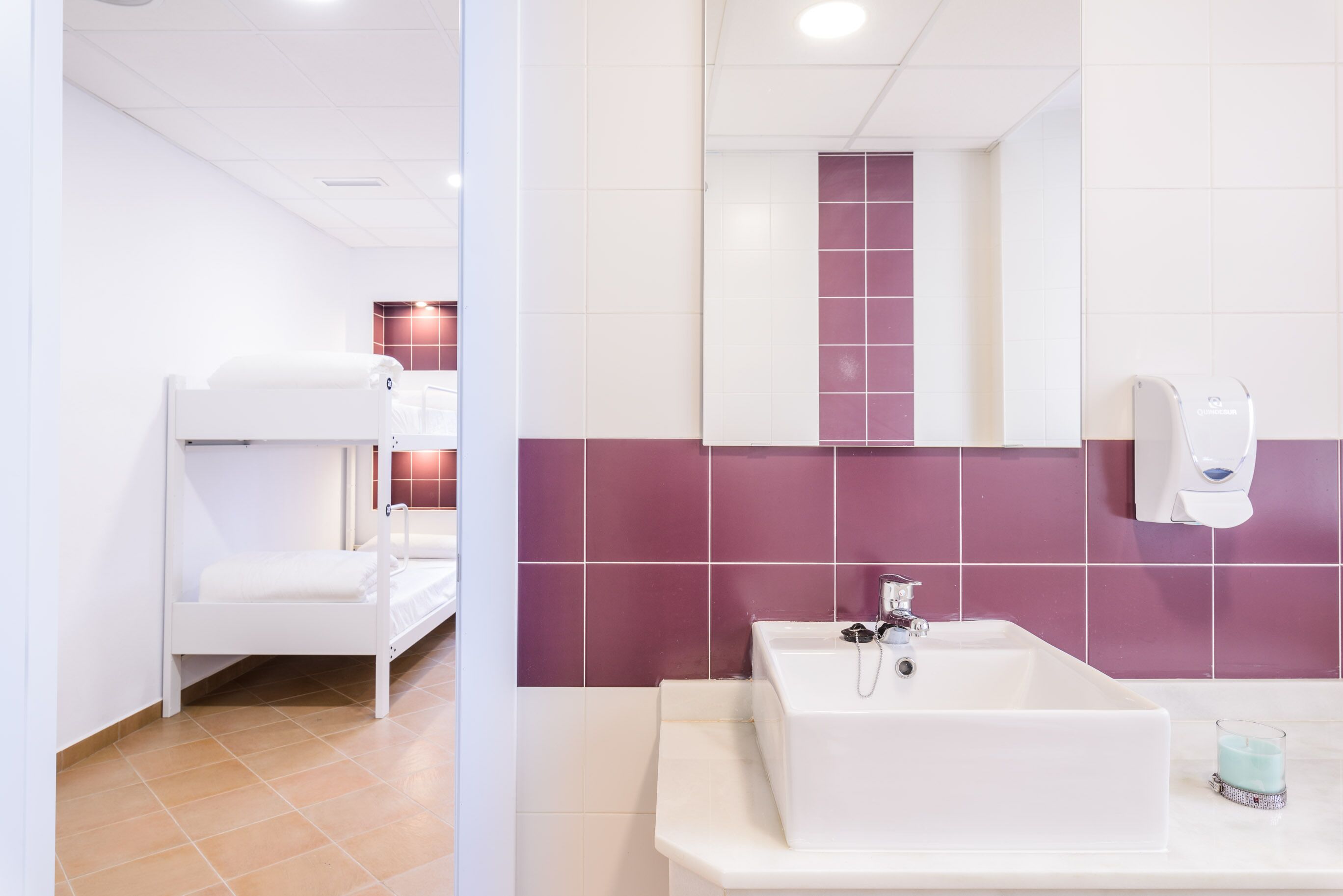 Un baño con un lavamanos blanco, azulejos morados, una bañera blanca y un secamanos blanco.