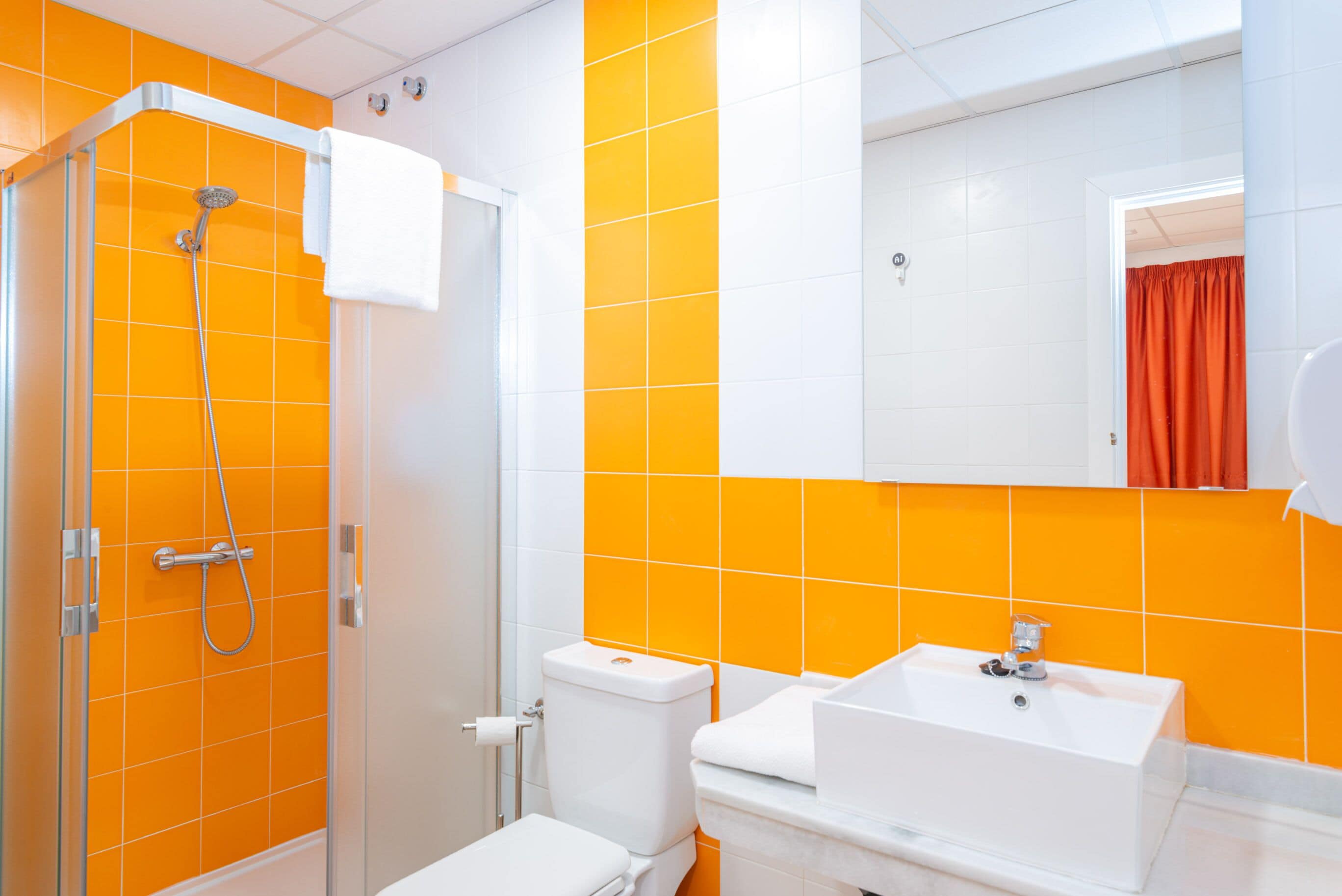 A bathroom with a glass shower enclosure, a white toilet, and a white sink with a mirror above it.