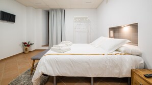 A neatly made bed with white linens, a bedside table with a remote control, and a wall-mounted TV. - Benarrabá Hostel (Benarraba)