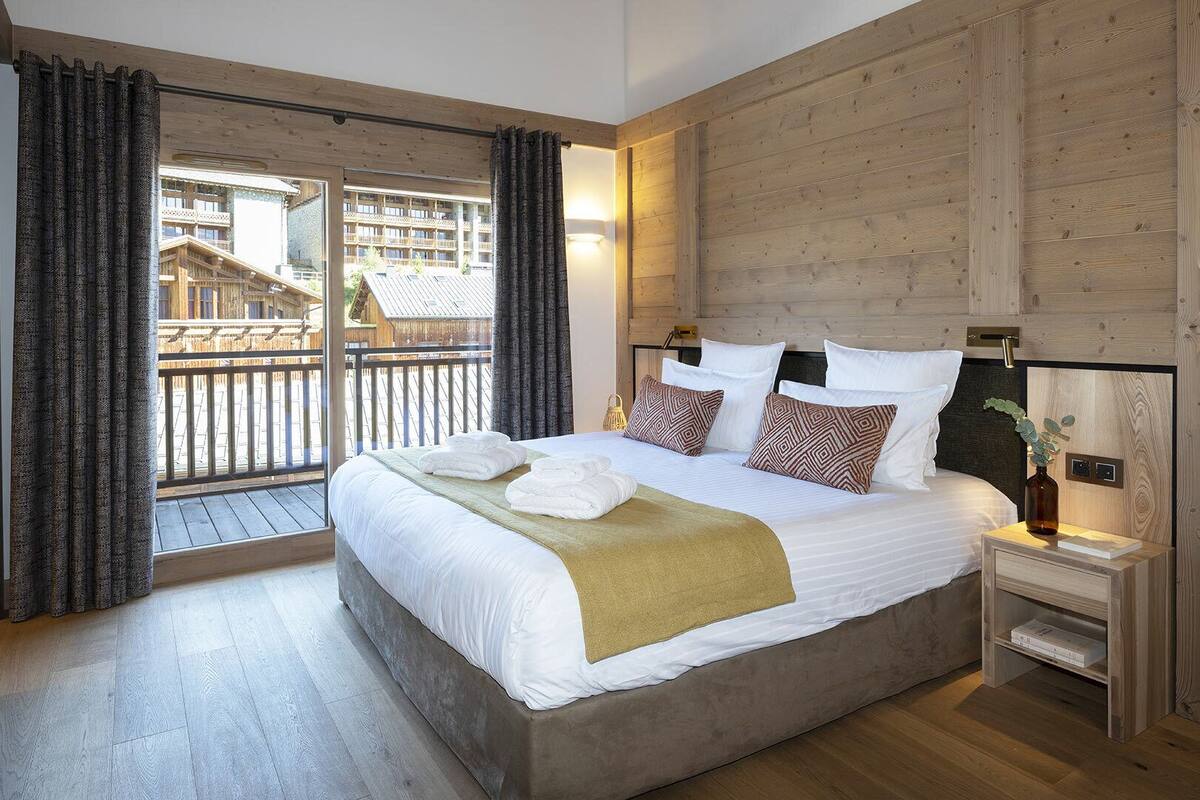Ein Schlafzimmer mit einem großen Bett, Holzwänden, einem Balkon mit Vorhängen und Blick auf Gebäude.