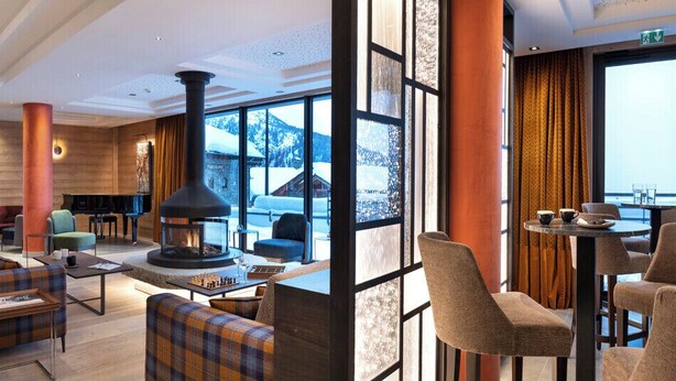 A modern lobby with a fireplace, seating areas, and large windows offering a view of the snowy mountains. - MGM Hôtels & Résidences – Hôtel Alpen Lodge (Montvalezan)