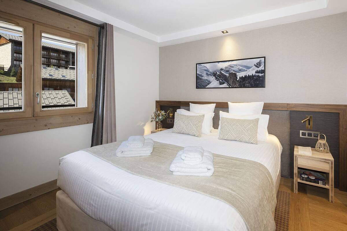 Ein Hotelzimmer mit einem großen Bett, einem Nachttisch, einem Fenster mit Vorhängen und einem gerahmten Bild an der Wand.