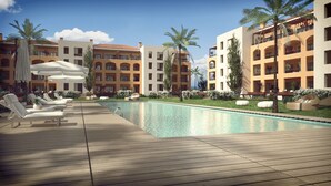 Zona junto a la piscina con sillones de descanso y una terraza de madera, rodeada de edificios de varios pisos con balcones y palmeras.