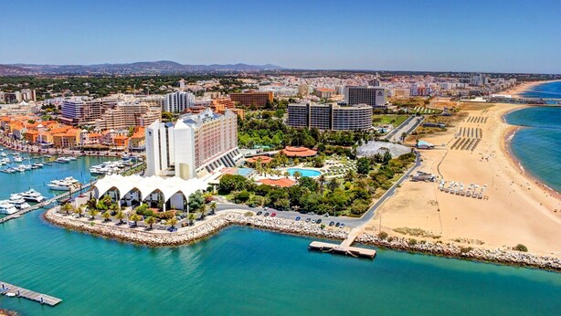 Un paisaje urbano costero con un puerto deportivo, un complejo turístico en la playa y edificios de gran altura.
