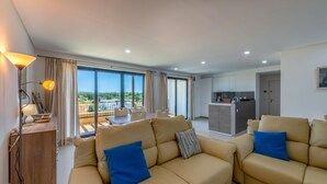 Amplia sala de estar con sofá y mesa de comedor, una kitchenette y ventanas grandes con vistas al exterior.