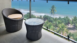 Un balcon meublé avec des meubles en osier, donnant sur une plage et l’océan.