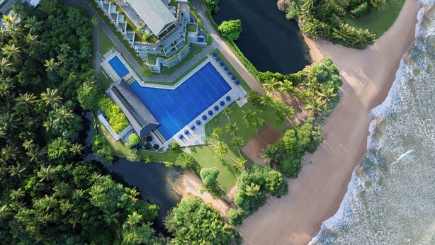 Vue aérienne d’un complexe hôtelier doté d’une grande piscine, d’un accès à la plage et d’une végétation luxuriante.