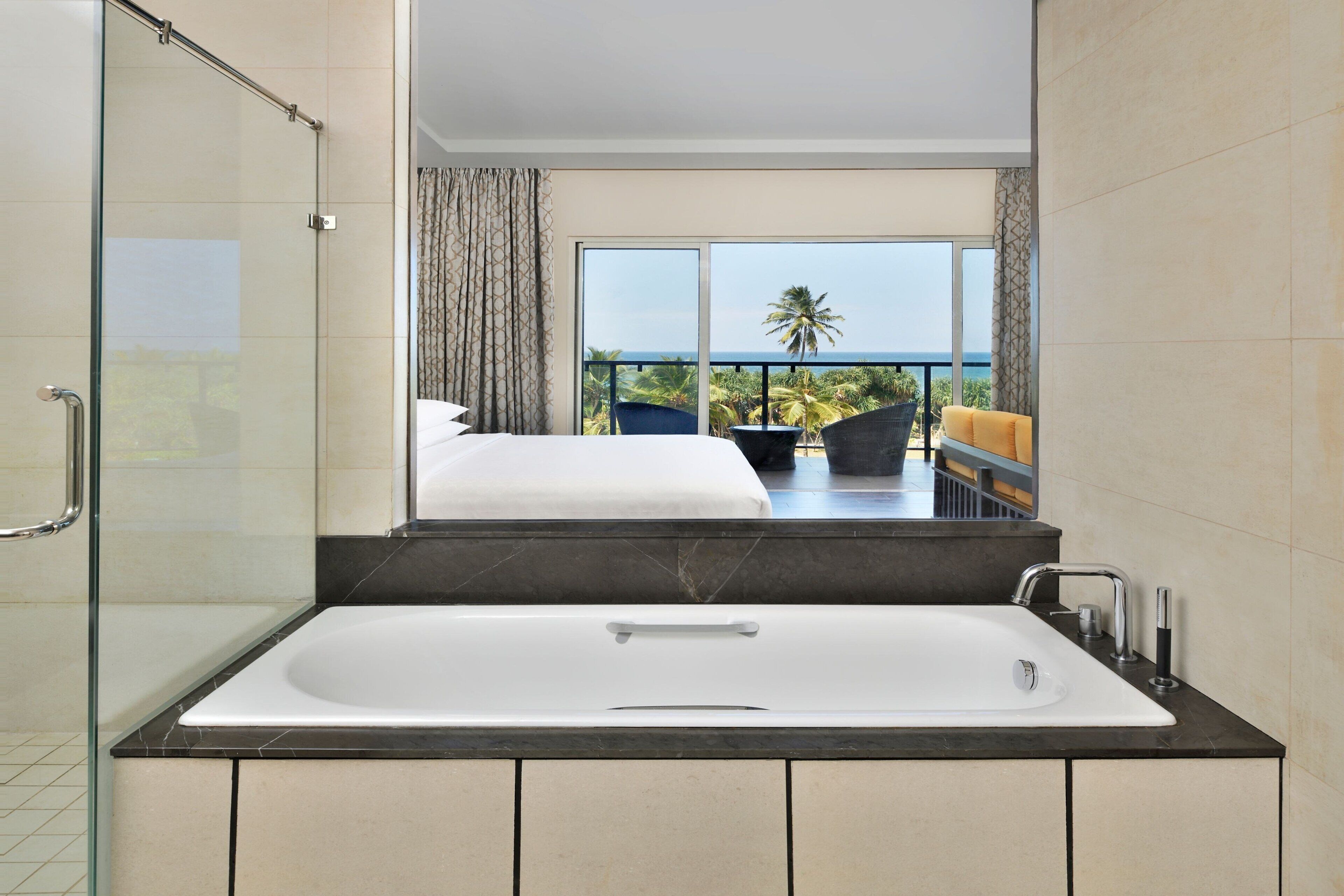 A modern bathroom with a glass-enclosed shower, a large bathtub, and a balcony with a view of the ocean.