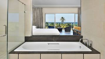 A modern bathroom with a glass-enclosed shower, a large bathtub, and a balcony with a view of the ocean.