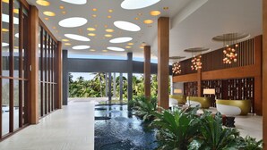 Un vaste espace intérieur abritant une piscine, agrémenté d’un plafond au design moderne, de grandes fenêtres et d’une végétation luxuriante.